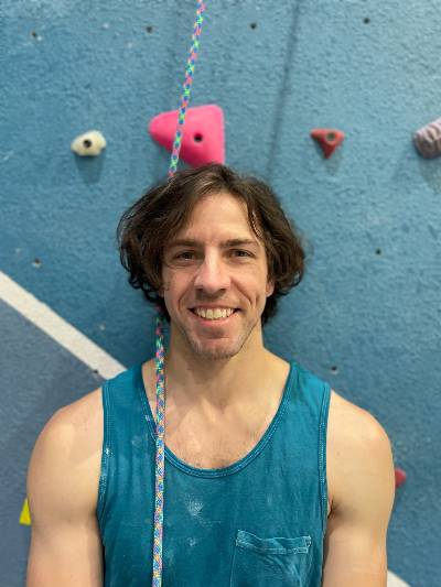 Joseph, smiling while standing in front of rock climbing wall