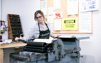 a student runs a letter press in the book arts studio