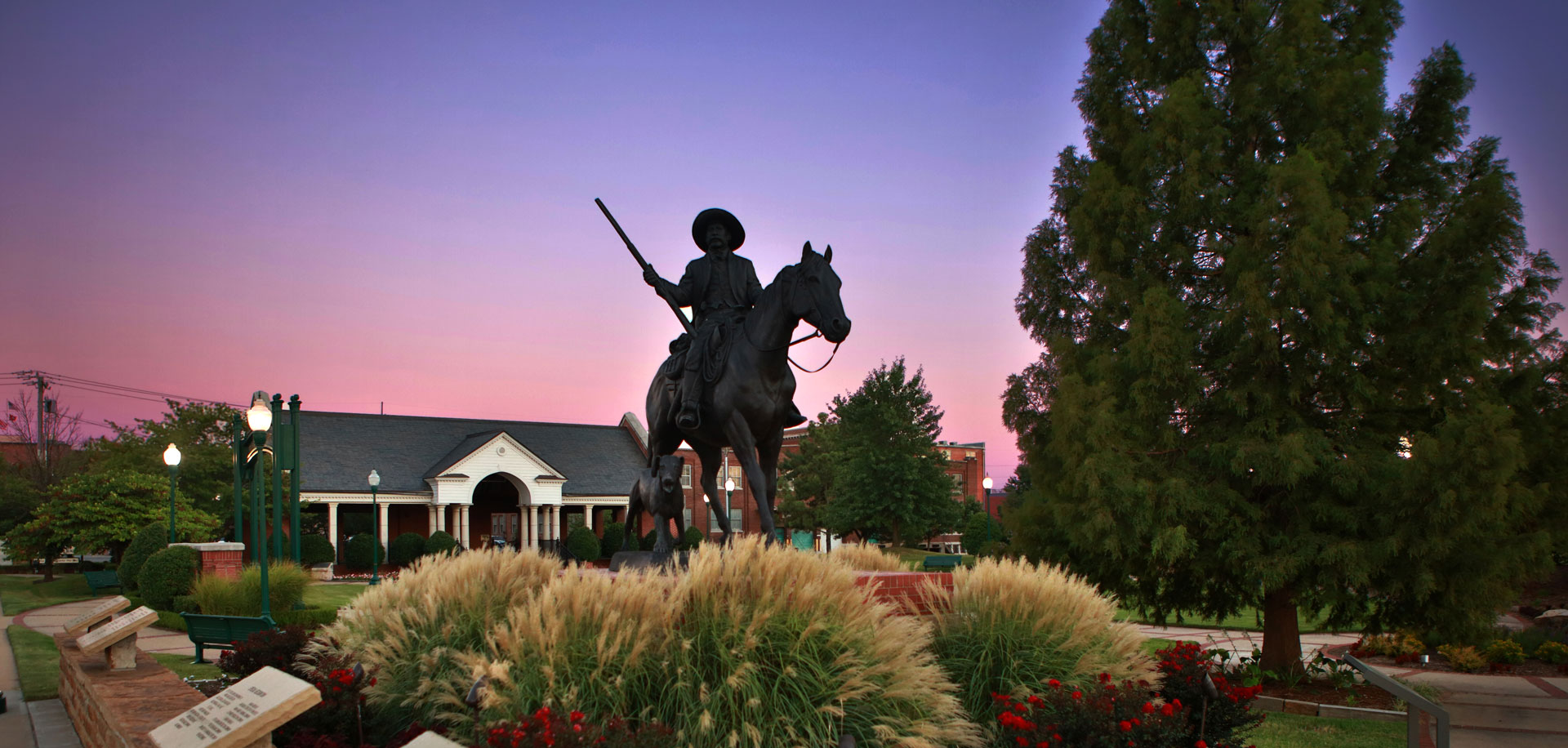 bronze statue of cowboy Bass Reeves sitting atop a horse with a purple dusk in the background