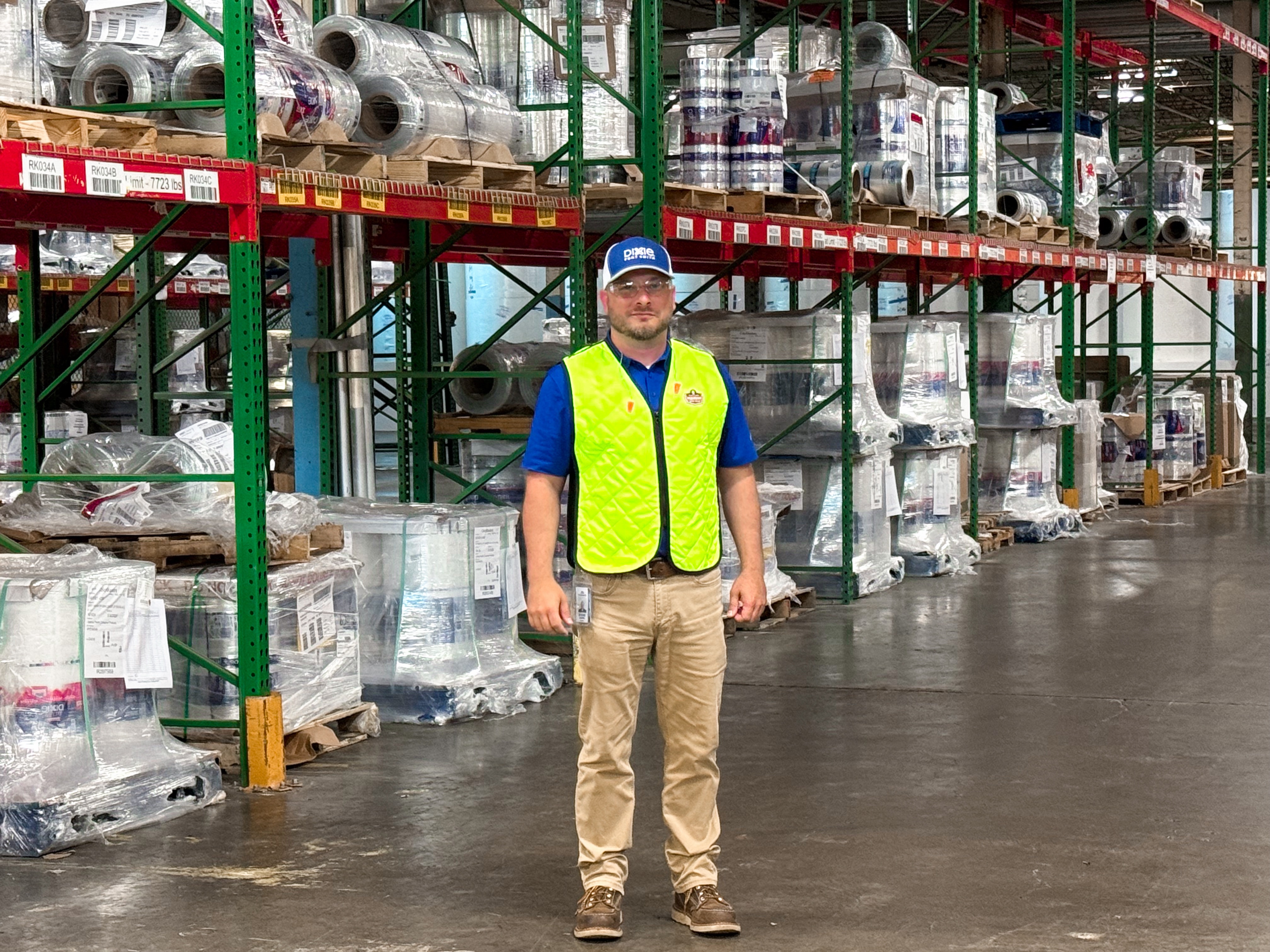 Man wearing a safety vest and safety glasses standing in front of full pallets in a warehouse