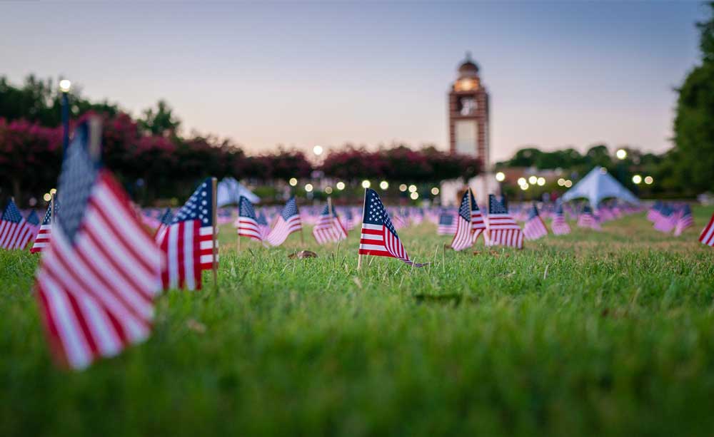 American Flags planted throughout the University of Arkansas - Fort Smith Campus Green with the Bell Tower in the background