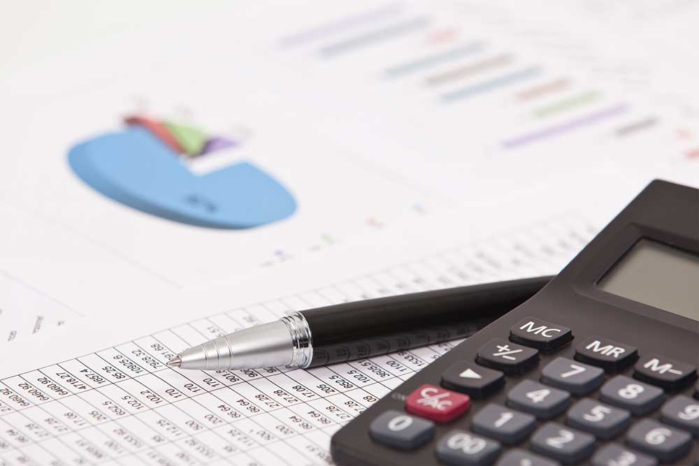 Stock image of a calculator and pen on top of accounting and finance documents.