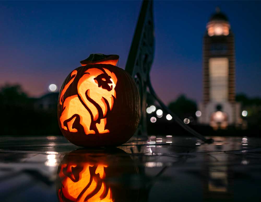 Pumpkin carved with UAFS logo with UAFS Belltower in the background