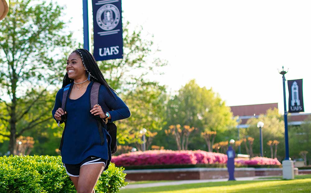 Student walks across the UAFS campus with her backpack and a smile