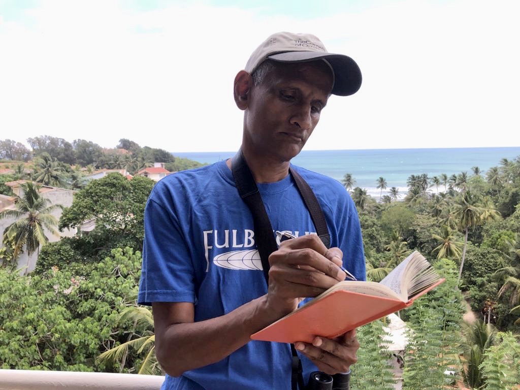 A man writes in a journal standing on an ocean hillside