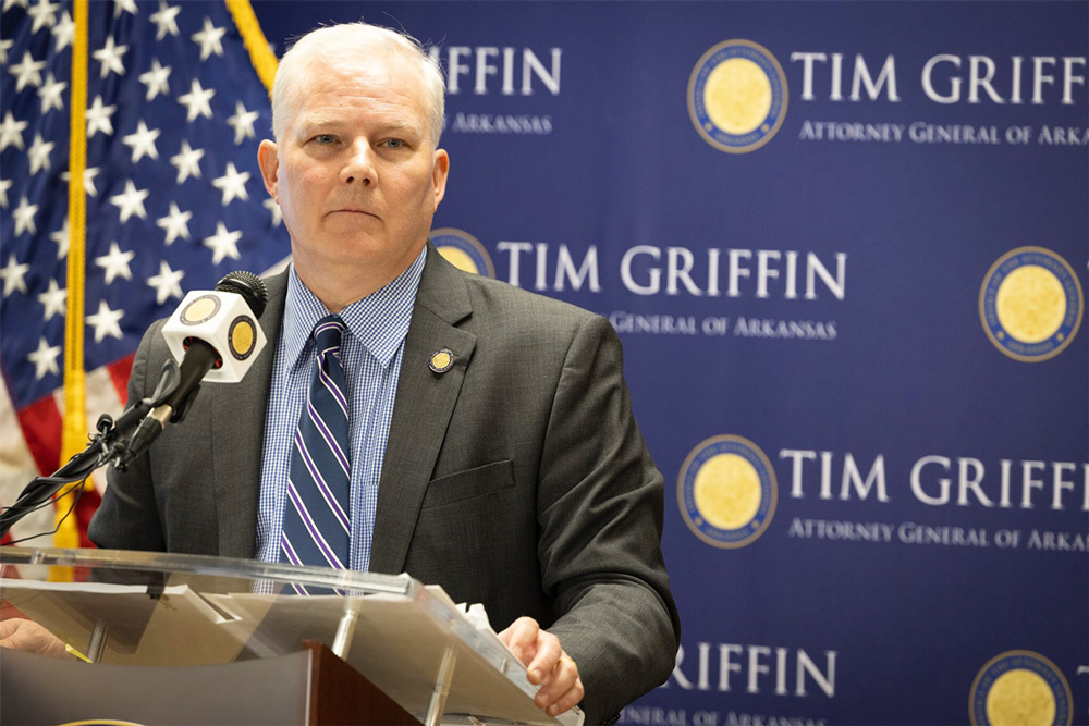 Arkansas Attorney General Tim Griffin speaks at a podium in front of a backdrop displaying the seal for the Attorney General of Arkansas.