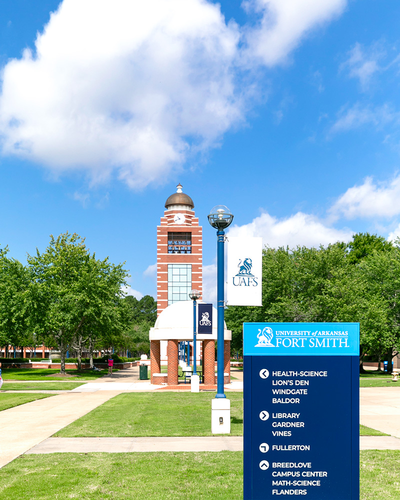 The UAFS Bell Tower sits in the background with a directional sign showing building locations sits in the foreground