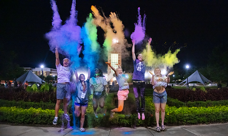 students toss colored powder at night on the UAFS campus