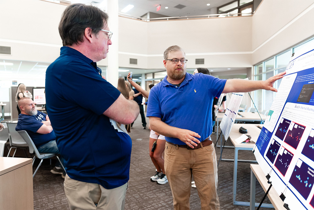 Christopher Edwards, center, shares his research into coral bleaching at the 19th Annual Student Research Symposium in UAFS's Boreham Library.