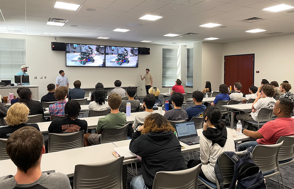 Front left to right: Cameron Taylor, Marco Garcia Montes, and Josue Martinez present "NumaWare: Process Automation Through Computer Vision and Robotics" to fellow students