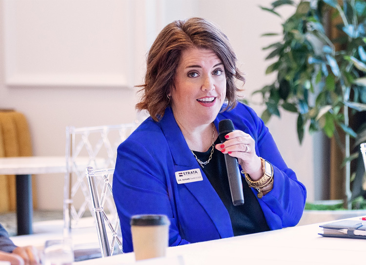Susan DeWoody talks into a microphone as part of a panel discussion representing Strata Leadership where she serves as president