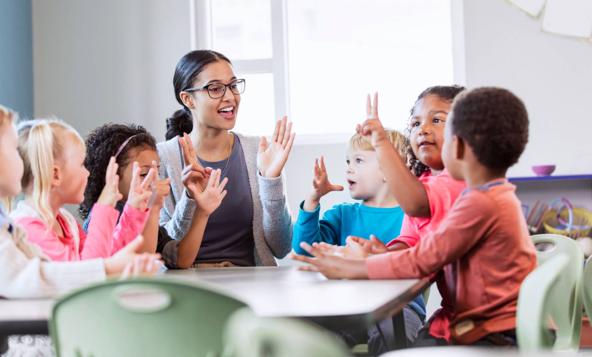 children in a pre-k classroom raise their hands
