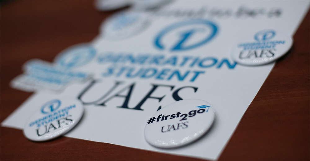 White buttons that read "#first2go - UAFS" and "First Generation Student - UAFS" sit on top of a first-generation sheet during a First-Generation Friday lunch event