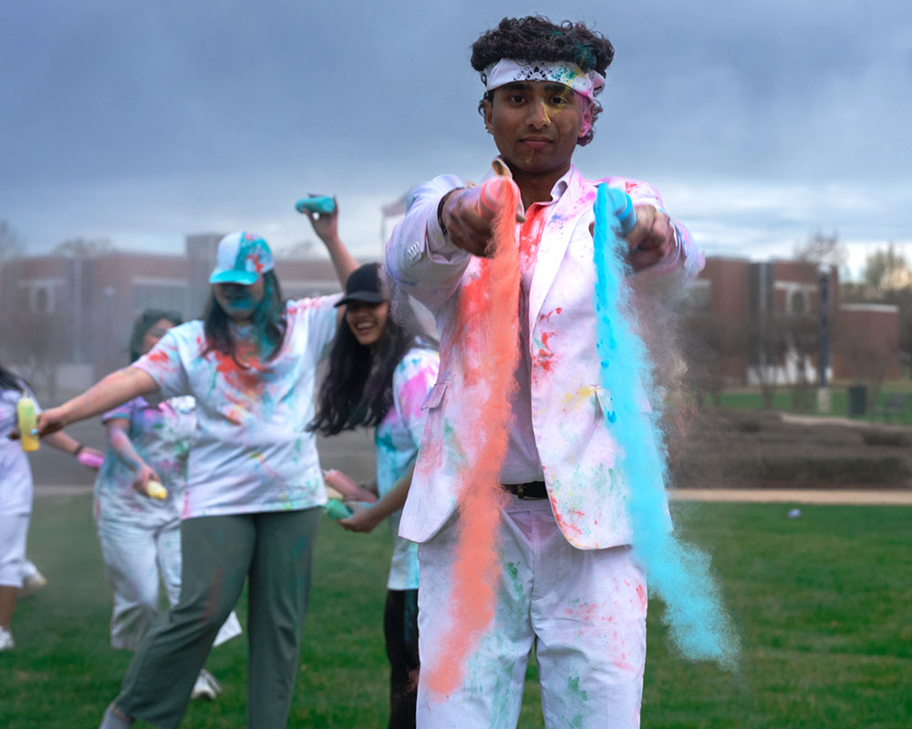 Desi Culture Club president Aravinda "Ara" Murali, wearing all white, throws red and blue colored powder for the Holi celebration on the UAFS Campus Green.