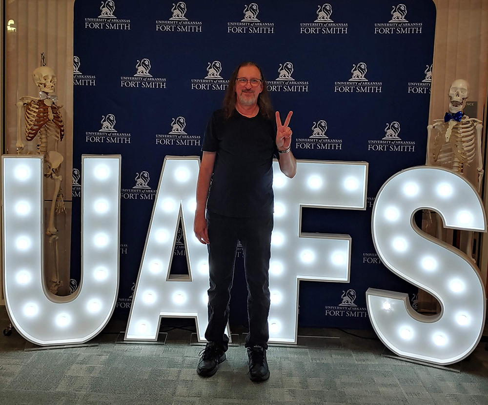 Dr. James Benjamin poses infront of a UAFS backdrop and light up letters spelling out UAFS.