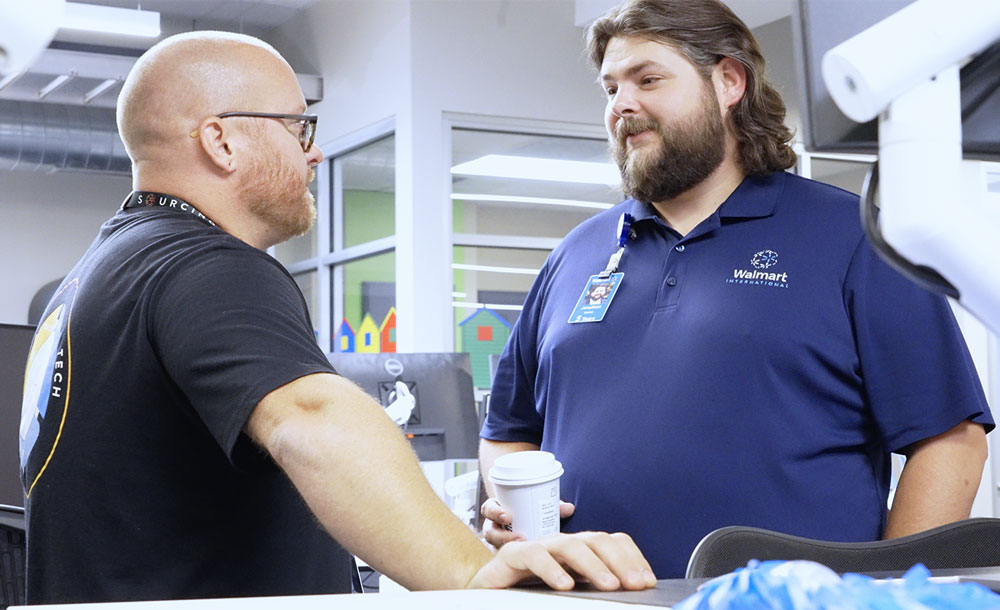 UAFS alum, Jon Walker, '17, talks to a co-worker at the Walmart International office