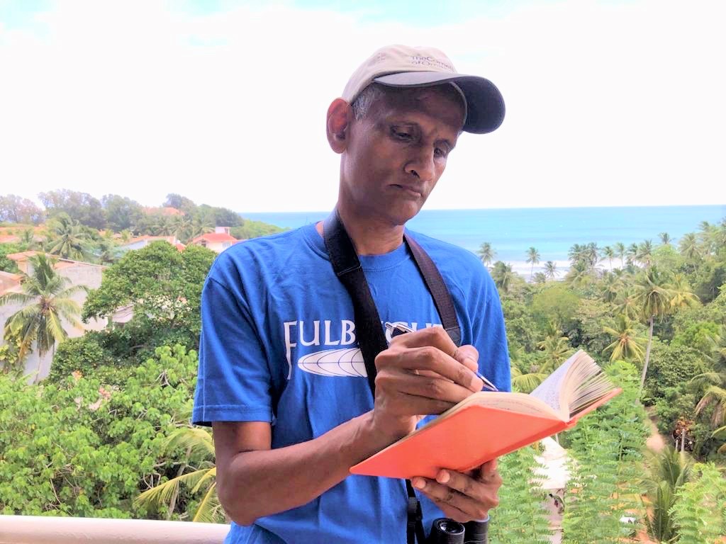 A man writing in a notebook against a tropical background