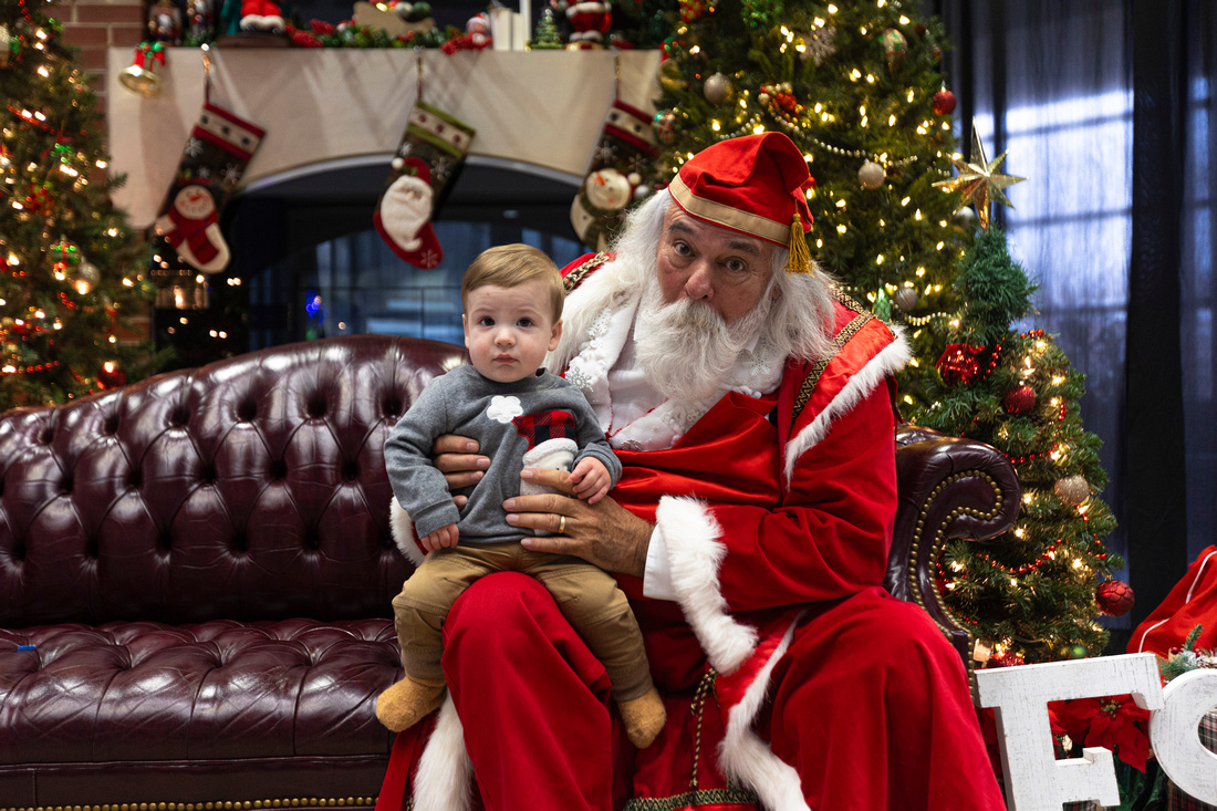 A small child in a Santa sweatshirt sits on the lap of Santa at UAFS, played by Harold Trisler, an alum of UAFS