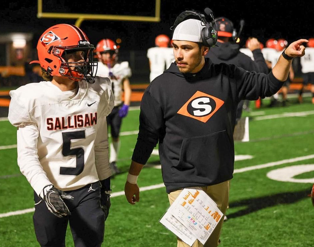 Logan Aguilera, class of '23, coaches a player at Sallisaw during a football game. Aguilera is a geography teacher at Sallisaw Middle School.