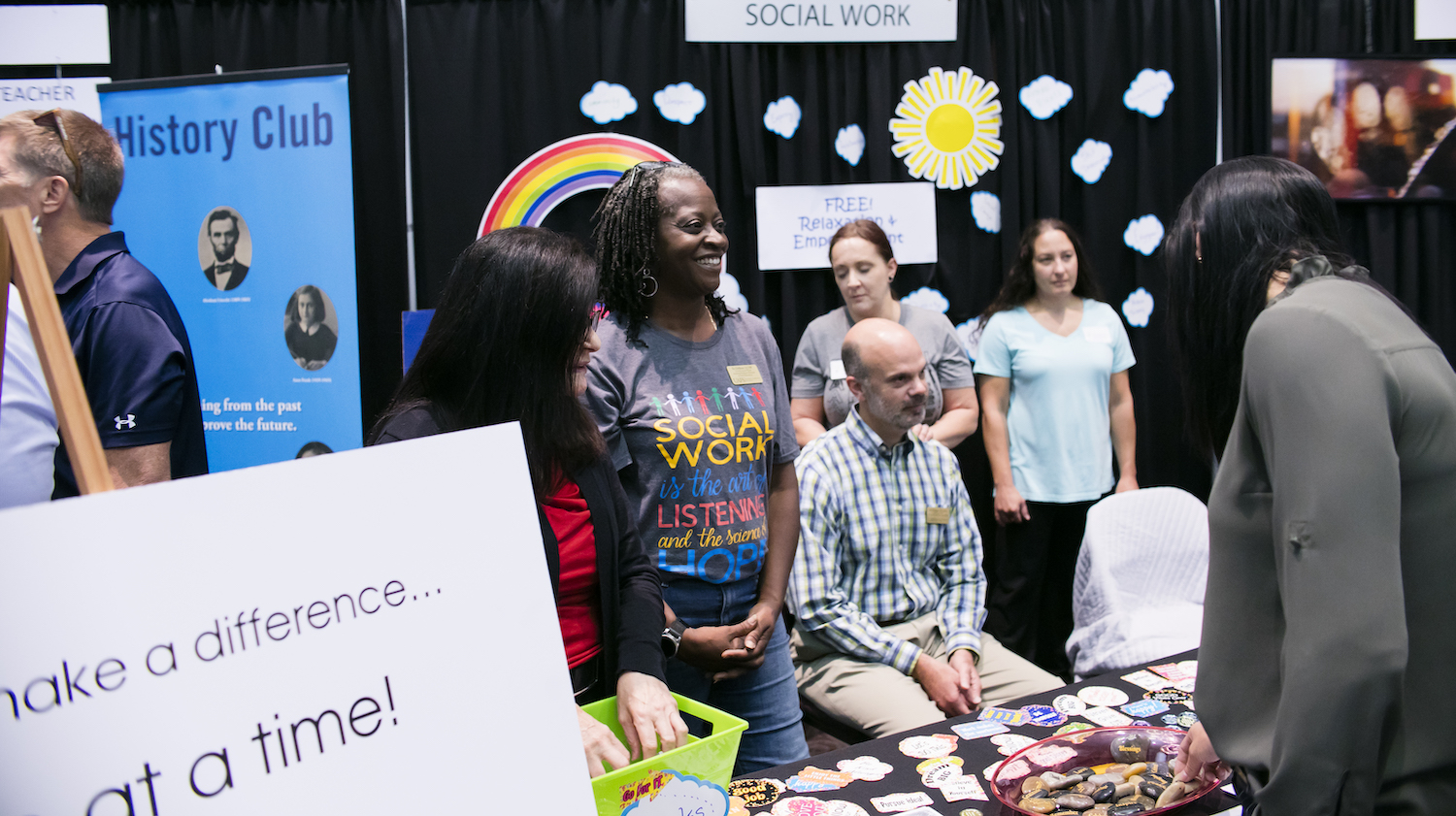 individuals stand in front of brightly colored tables at a majors expo
