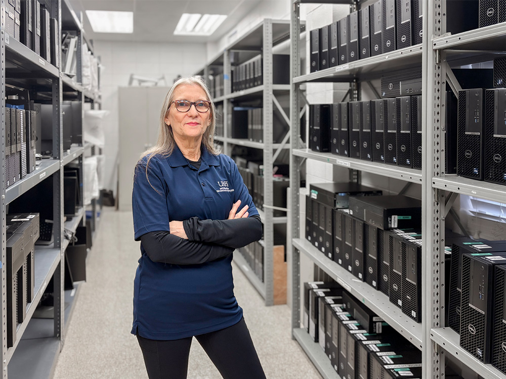 Mary Miller stands in the UAFS IT office surrounded by shelves filled with PCs