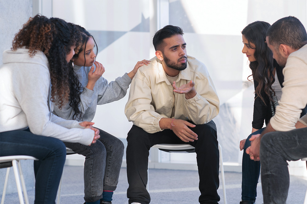 A group of students console a classmate while he is being vulnerable.