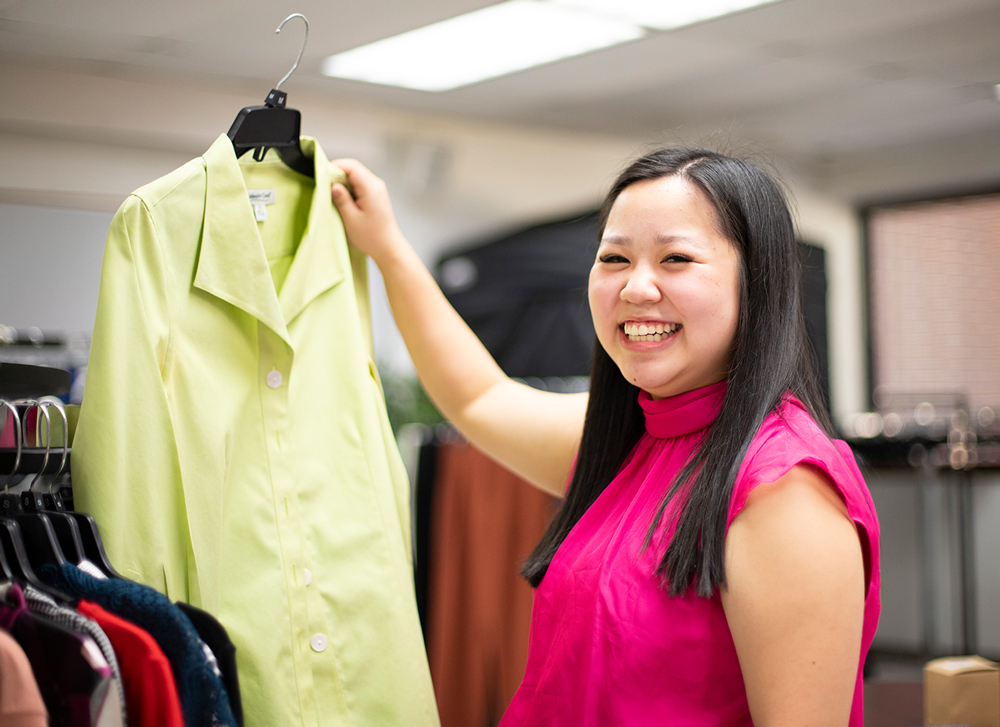 Natalie Chuong, a UAFS junior business administration major, smiles for the camera as she hands up a green blouse in the Babb Center for Career Services' Suit Up Studio. A place where students can obtain new or gently used professional attire for free.