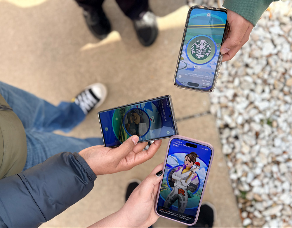 Three members of The Pokémon Guild at UAFS hold out their phones together while playing Pokémon GO.