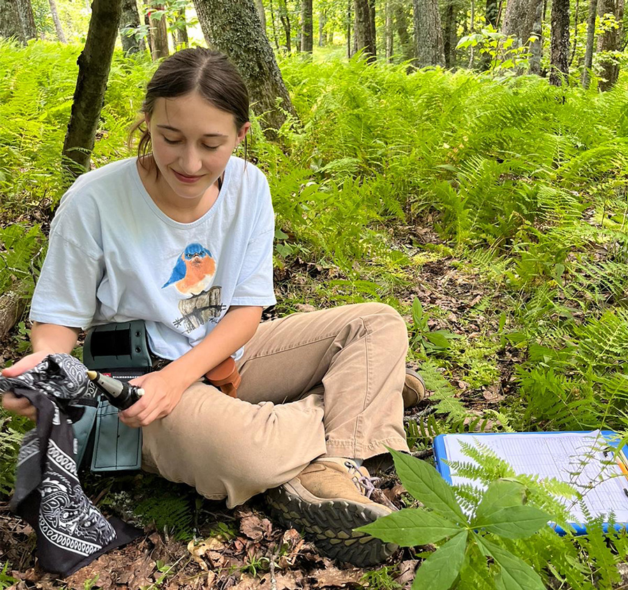UAFS senior biology student, Shelby Zink, wipes off equipment while sitting in a forested area while on a research expedition.