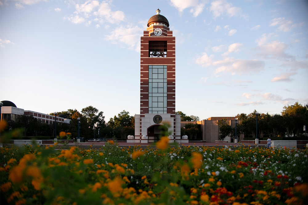 UAFS Bell Tower at sunset, yellow, red, and white flowers from the UAFS Campus Green garden are in the foreground