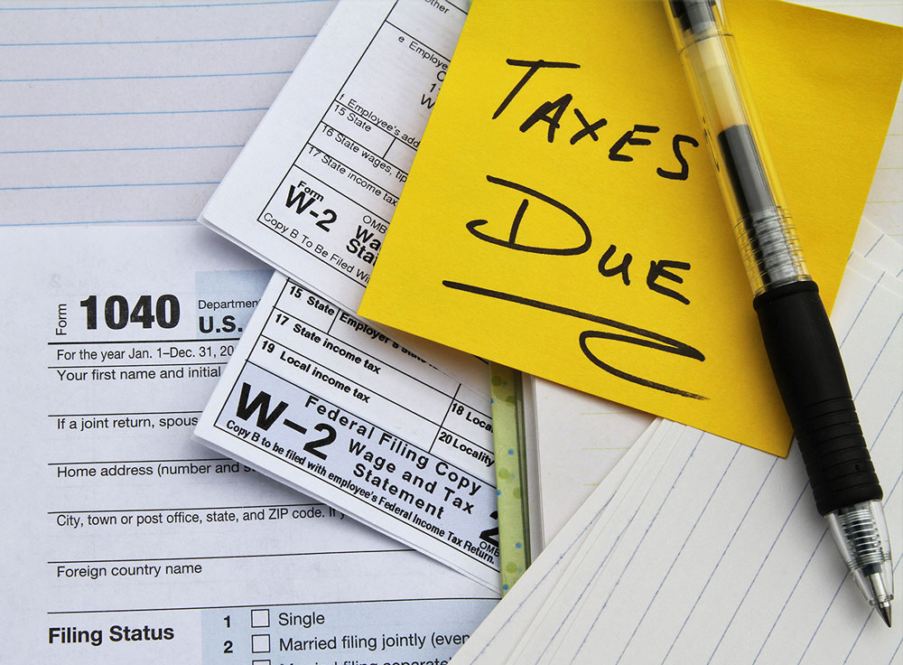 Image of a yellow sticky note that says "Taxes Due" on top of a blank W-2 and blank 1040
