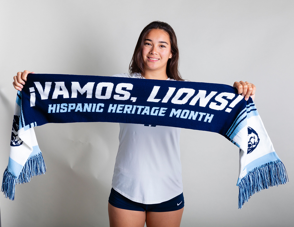 UAFS Volleyball player holds up a Hispanic Heritage Month commemorative scarf that reads, "¡Vamos, Lions!"